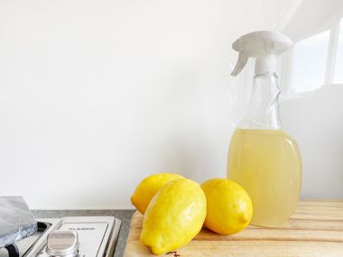 Selbstgemachter Reiniger in einer Plastiksprüflasche und davor liegen 3 Zitronen auf dem Tisch